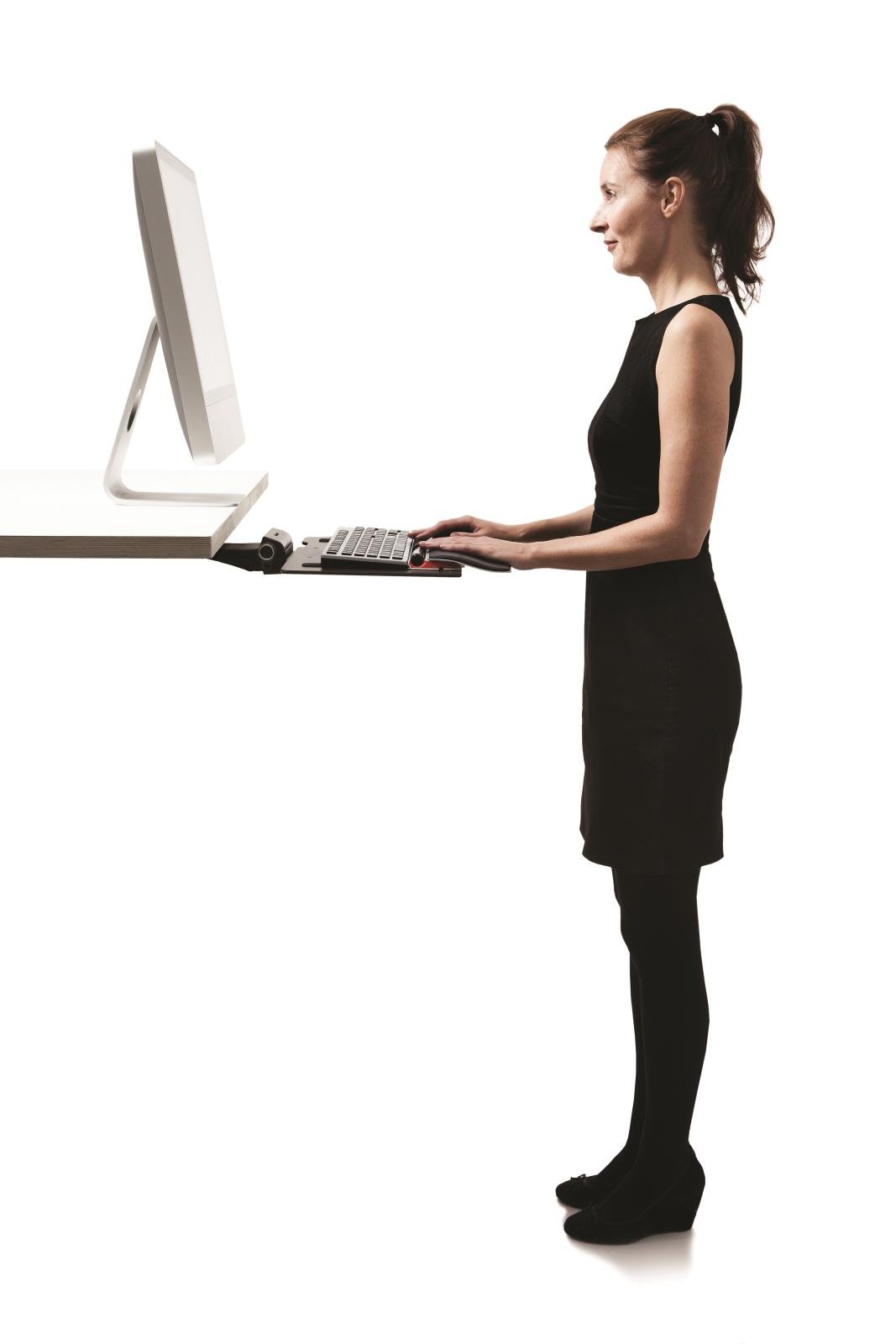 Kvinna står vid ett skrivbord med en ergonomisk mus och datorskärm, arbetar vid ett höj- och sänkbart skrivbord