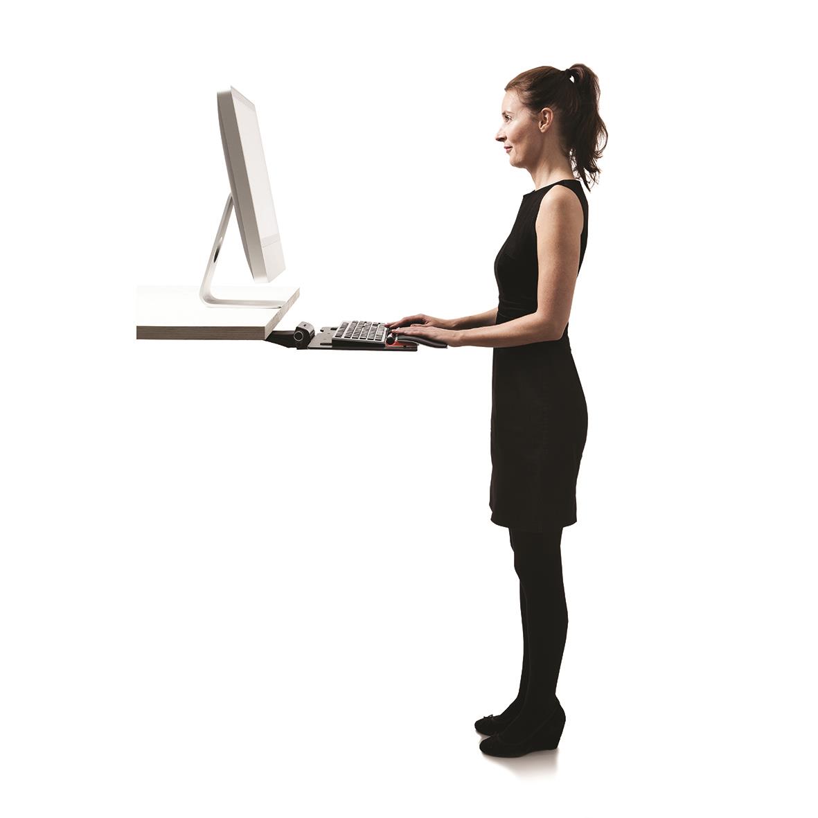 Kvinna står vid ett skrivbord med en ergonomisk mus och datorskärm, arbetar vid ett höj- och sänkbart skrivbord