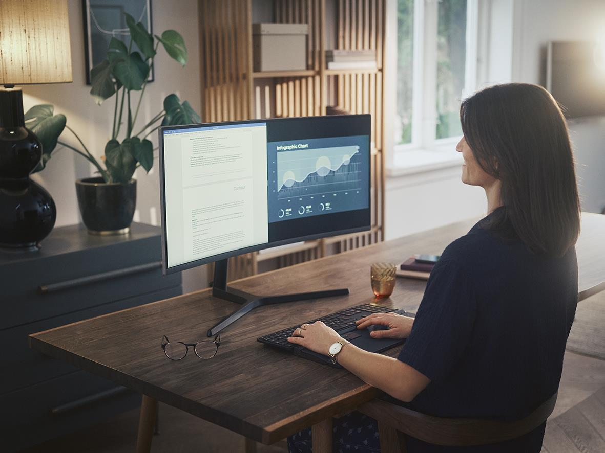 Kvinna använder tangentbord och dubbelbildskärm på arbetsbord i hemmet