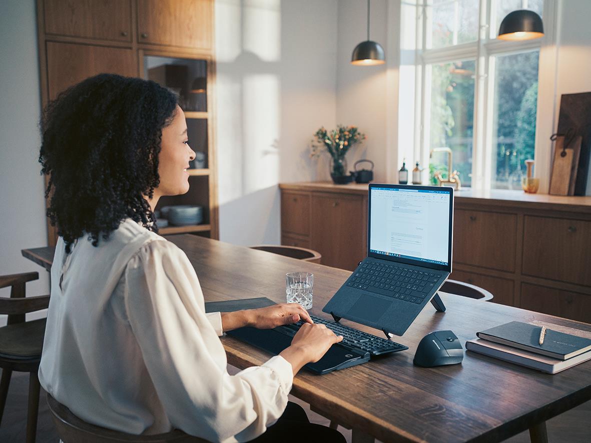 Kvinna arbetar vid skrivbord med ergonomisk mus och laptop i ett ljust hemkontor