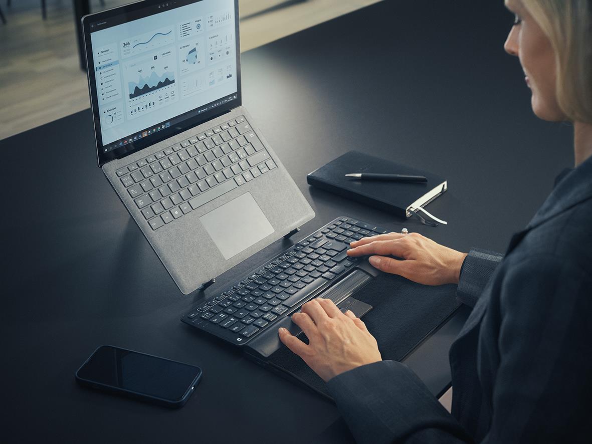 Person använder ergonomisk trådlös mus och tangentbord vid laptop med grafiska data på skärmen