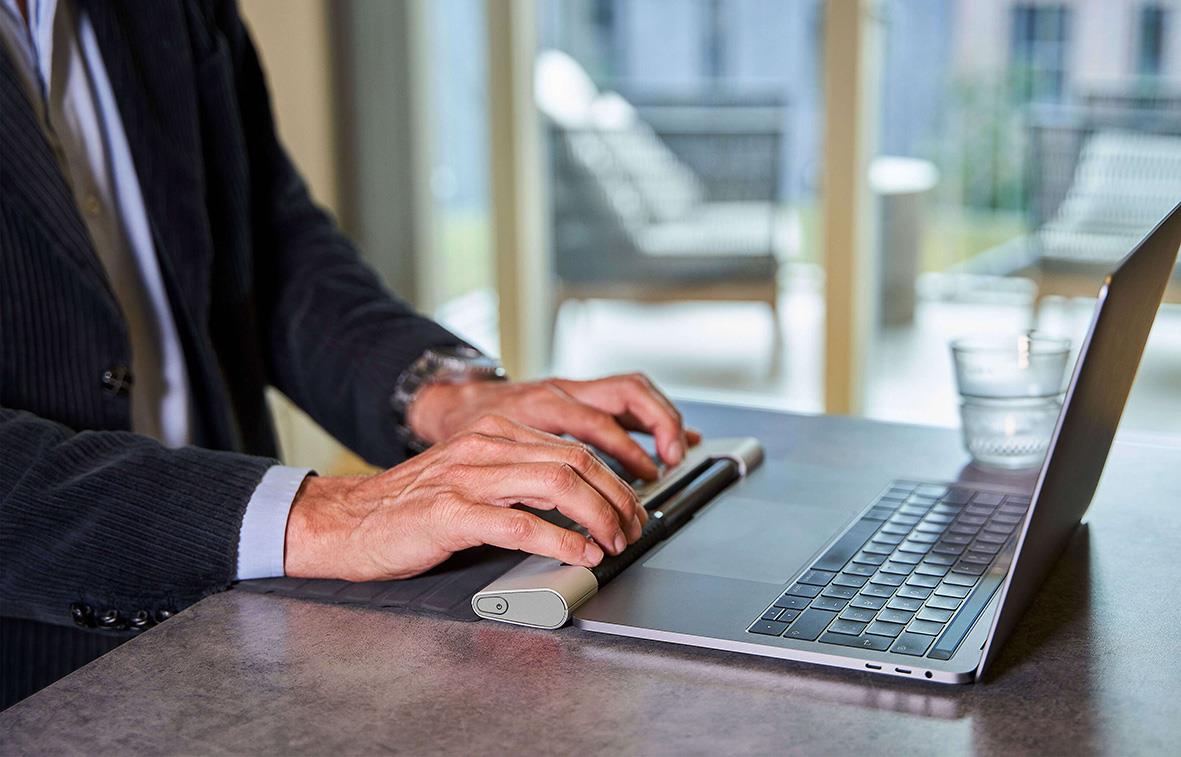 Person använder ergonomisk mus och laptop på skrivbord i kontorsmiljö