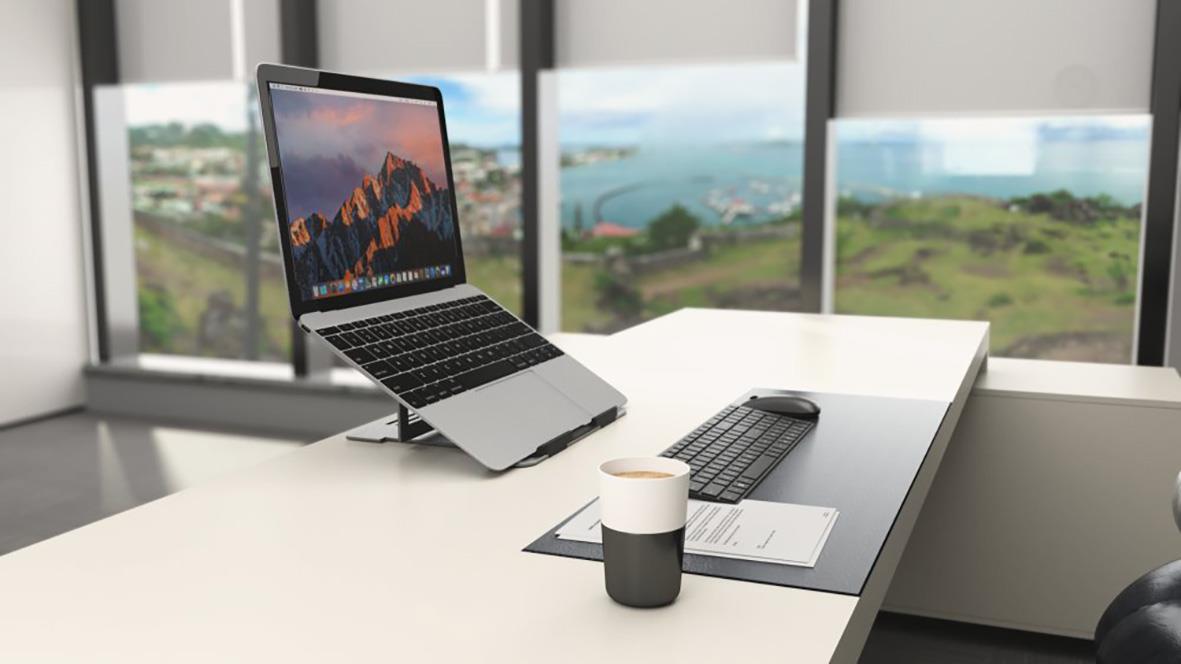 Justerbart laptopstöd Kensington EasyRiser på ett skrivbord med laptop, tangentbord, mus och kaffekopp framför stora fönster med utsikt