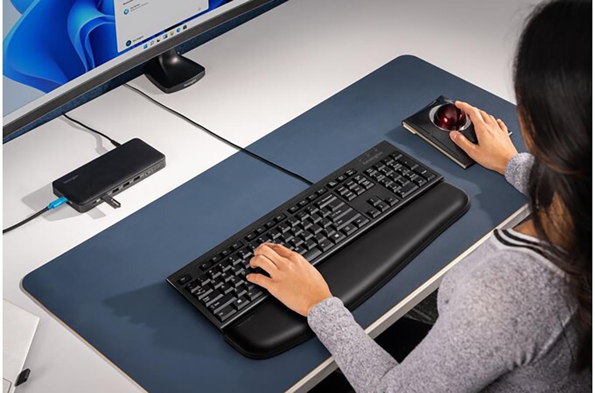 Person använder ett svart tangentbord och mus på ett skrivbord med en datorskärm