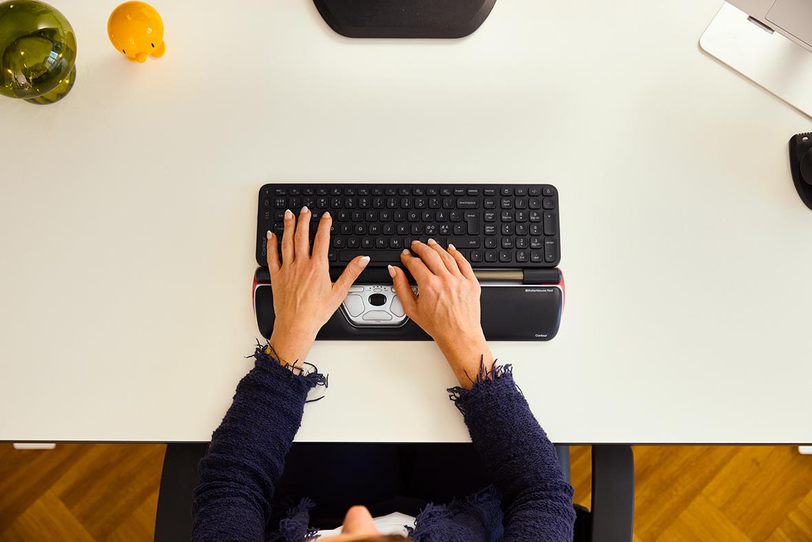 Person som använder ett trådlöst tangentbord på ett skrivbord med olika kontorsprylar