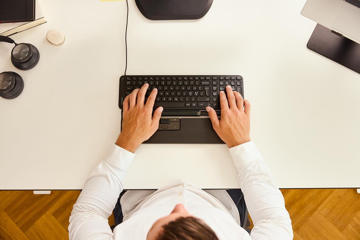 Person som skriver på ett mellanstort tangentbord med sladd, sett ovanifrån