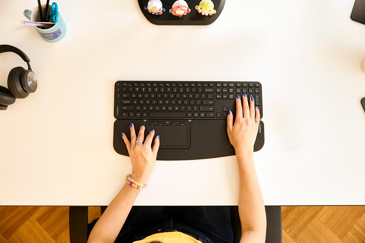 Person som använder ett trådlöst fullstort tangentbord på ett skrivbord med några kontorssaker