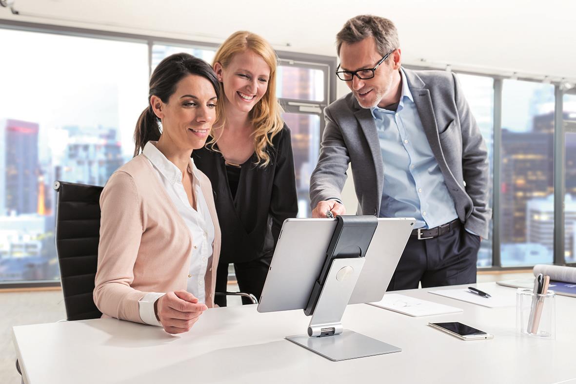 Tre personer i ett kontorsmöte använder en surfplatteställning på ett skrivbord