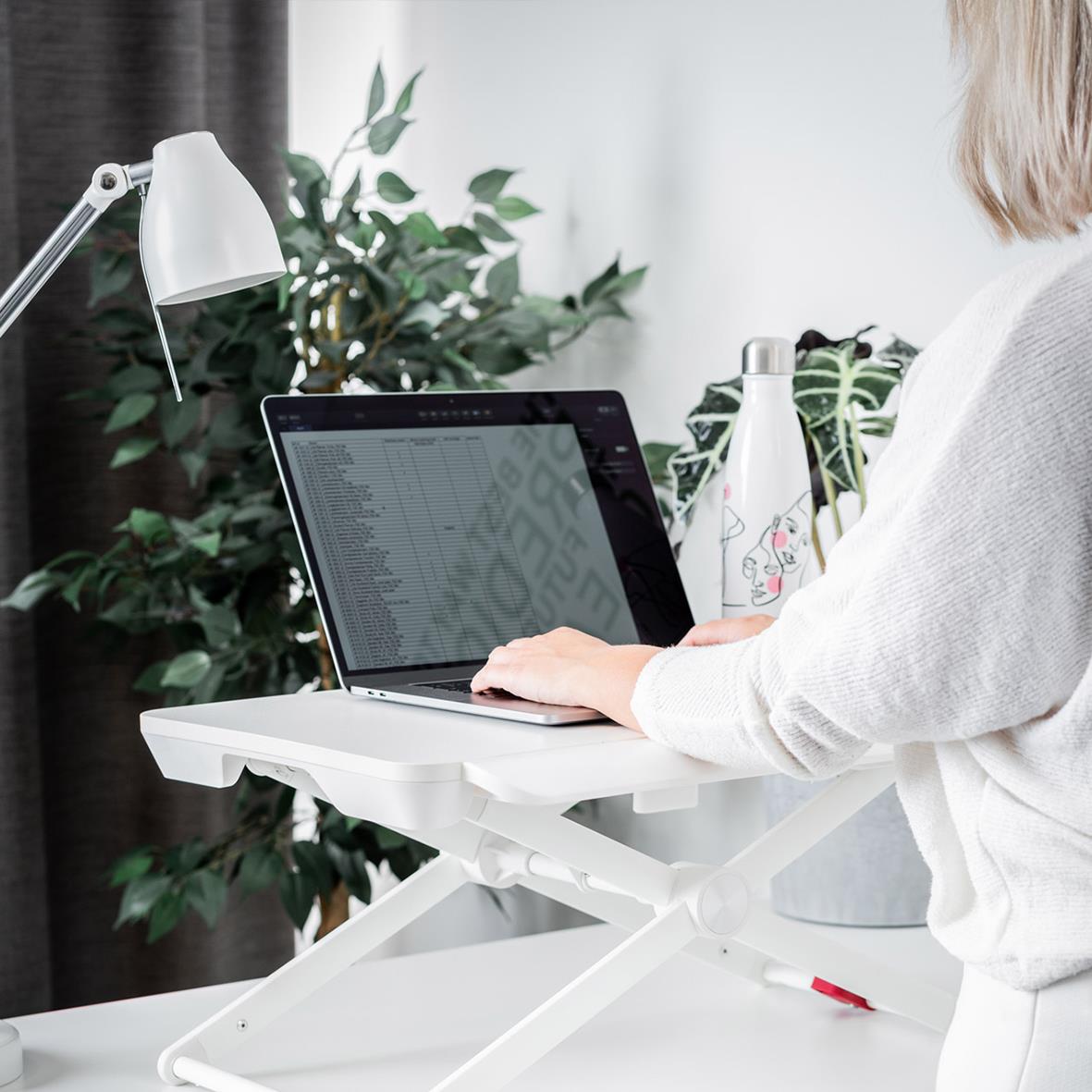 Portabelt justerbart ståbord med laptop och arbetslampa i ett hem- eller kontorsutrymme