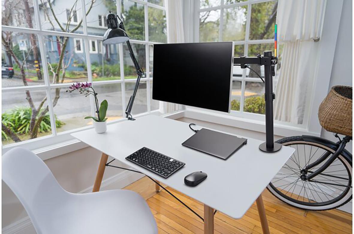 Arbetsplats med monitorarm, dator, tangentbord, mus och cykel i ett ljust rum med stora fönster