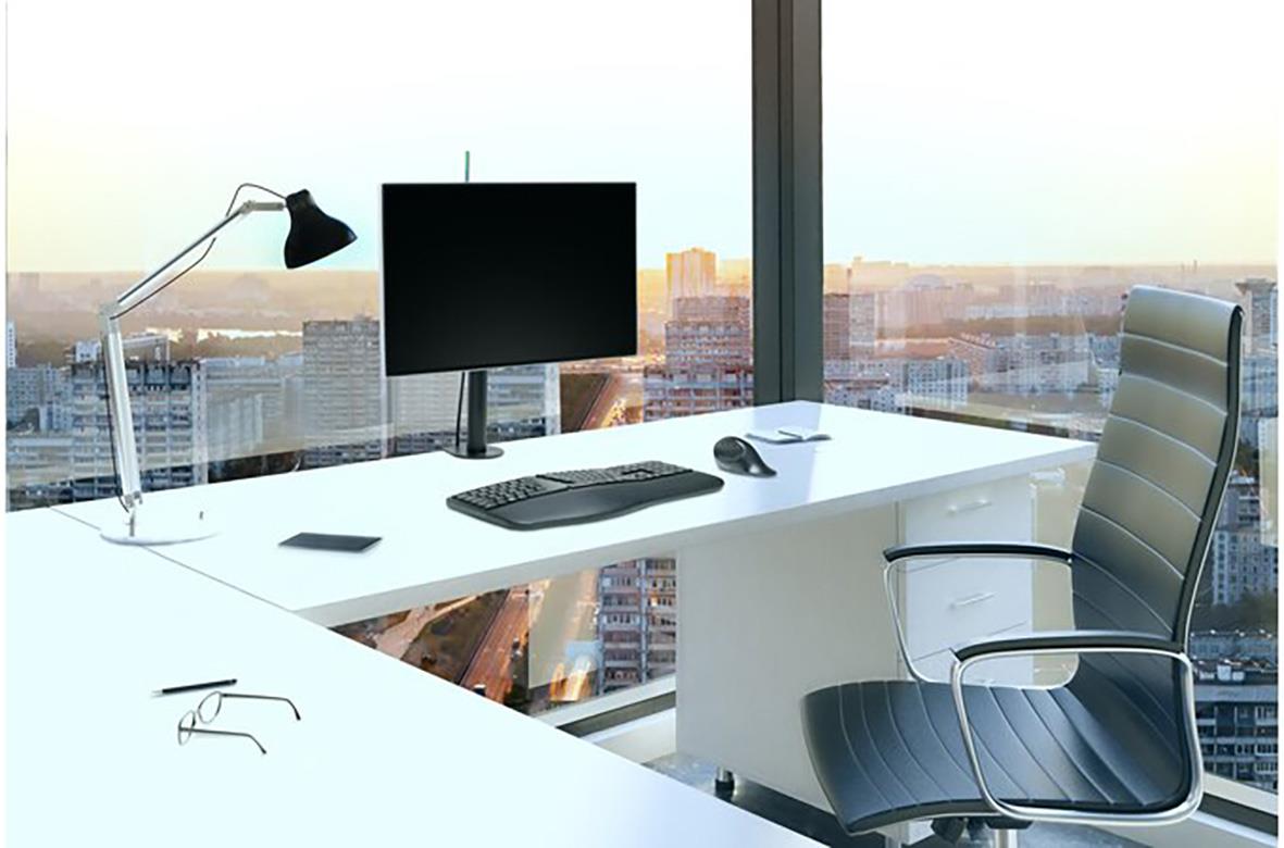 Kontorsbord med monitorarm, datorskärm, tangentbord, mus, skrivbordslampa och kontorsstol framför stor fönster med stadsvy