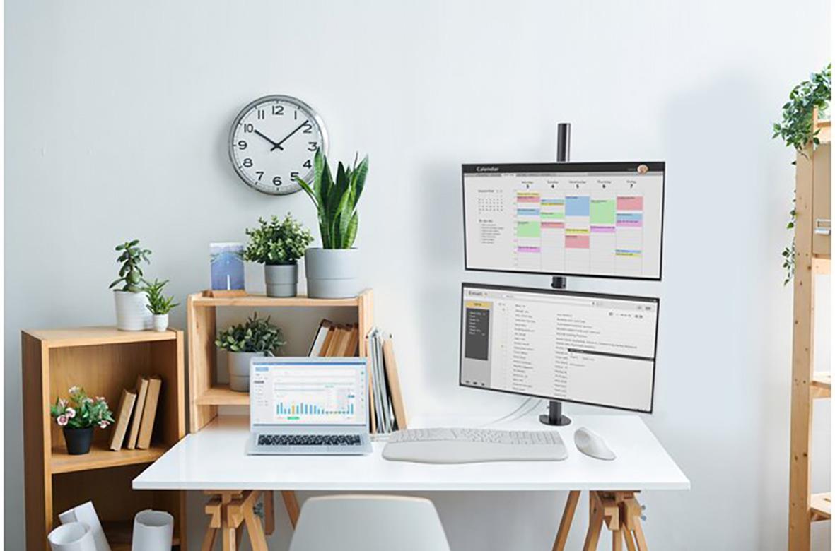 Arbetsplats med monitorarm, växter och bokhyllor på vit skrivbord i ett ljust rum
