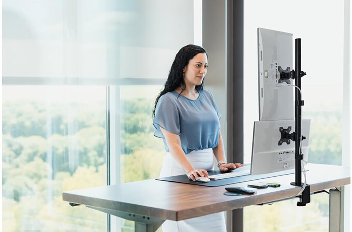 Kvinna använder en vertikal monitorarm på ett skrivbord med en stor skärm framför sig