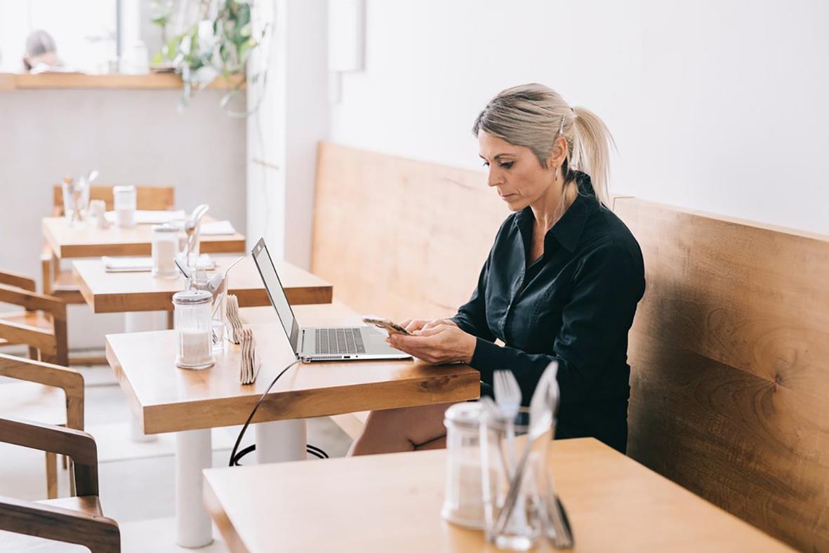 Kvinna använder mobil på cafébord med laptop och vattenflaskor i bakgrunden