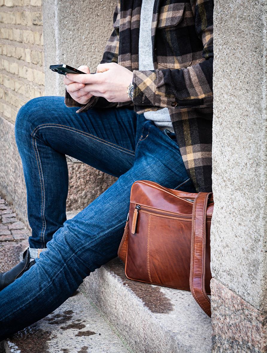 Person som sitter mot en vägg med en iPadväska i skinn Cognac bredvid sig