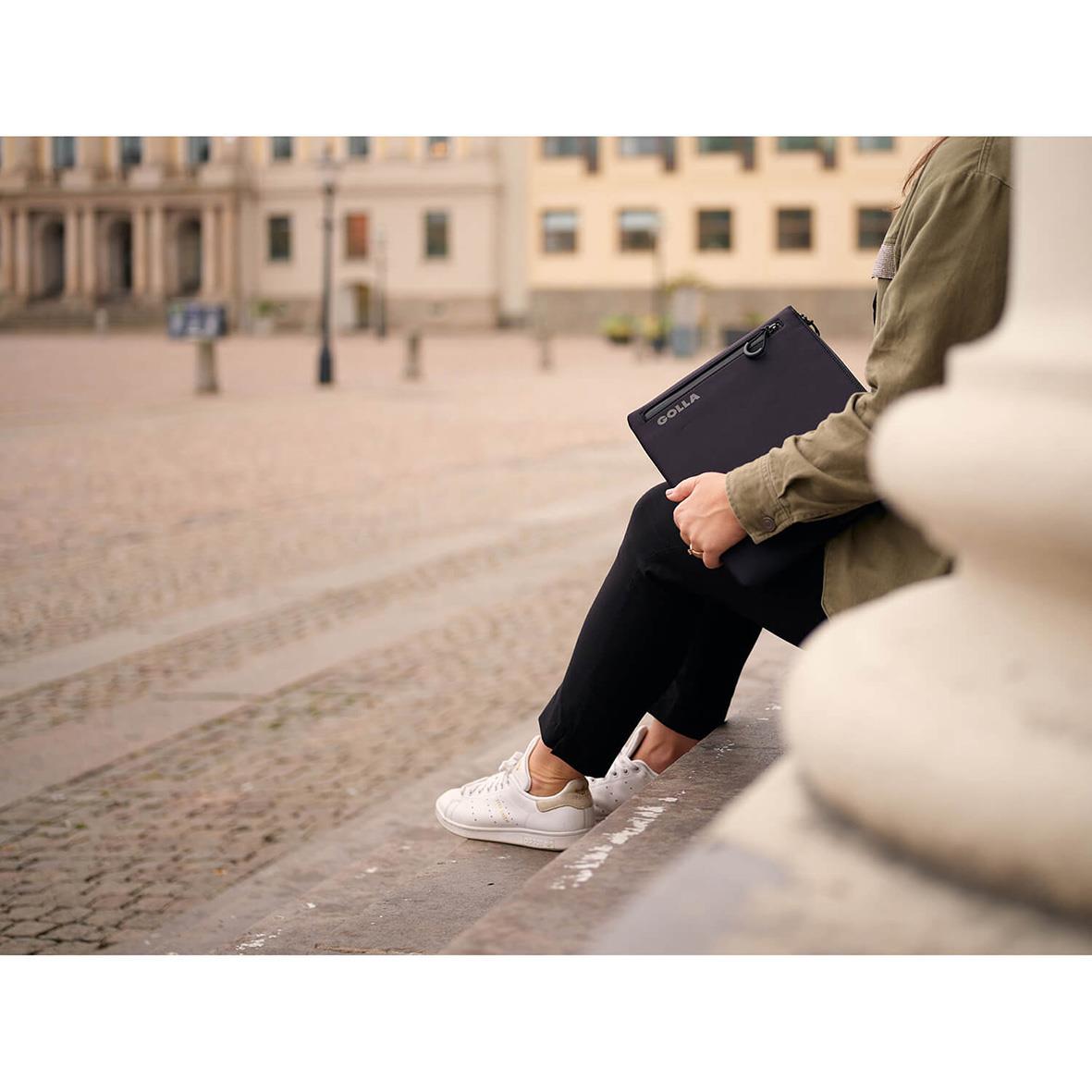 Person som sitter på en bänk och håller ett svart Golla Metro neopren datorfodral för 13 tum