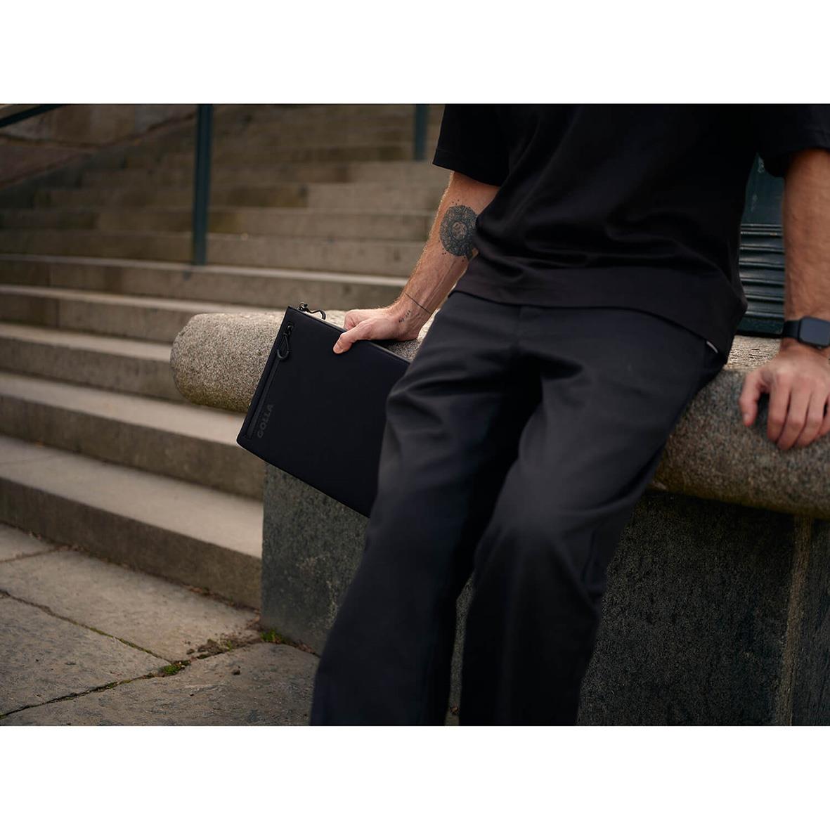 Person som sitter på en bänk med ett svart neopren datorfodral för 13 tum