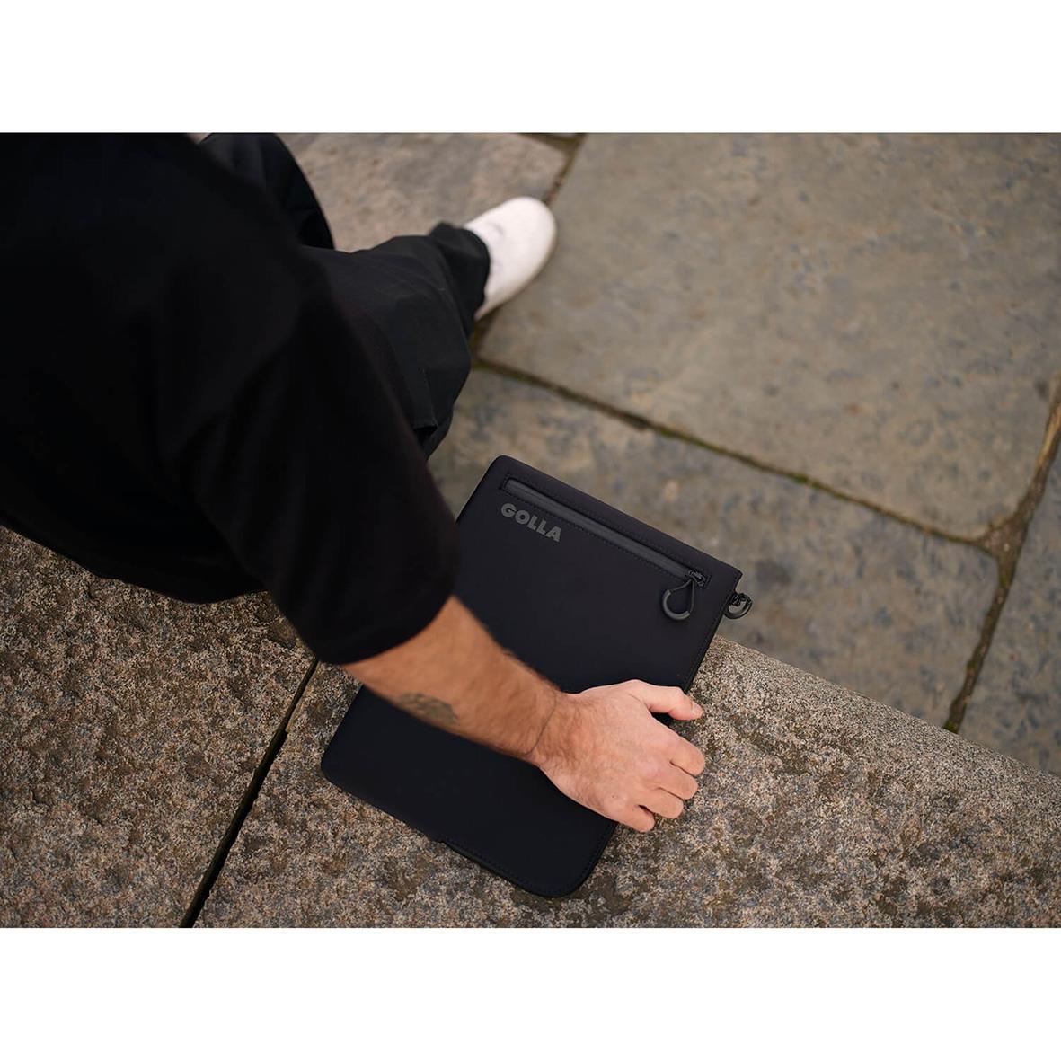 Person håller ett svart Golla Metro neopren datorfodral för 13 tum på en stenbänk utomhus