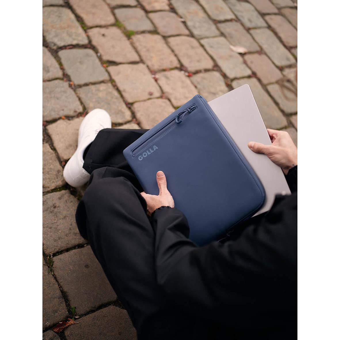 Person som håller ett blått neopren datorfodral Golla Metro Petroleum 13 tum medan de sitter på en stenbelagd yta