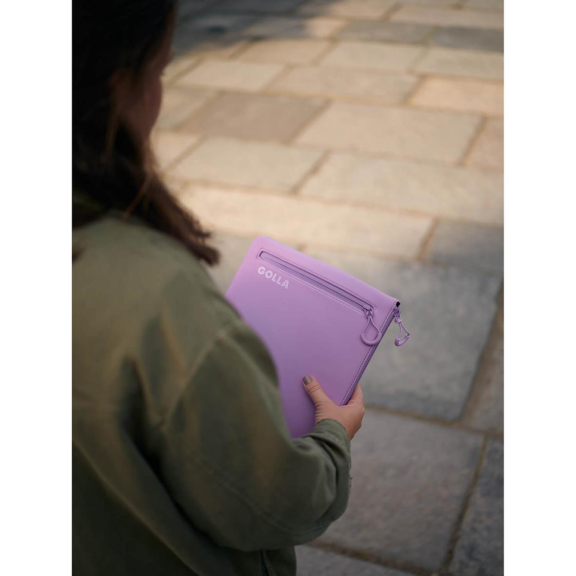 Person håller ett lila neopren datorfodral från Golla Metro Pastel Lilac för 13 tum utomhus på gatsten