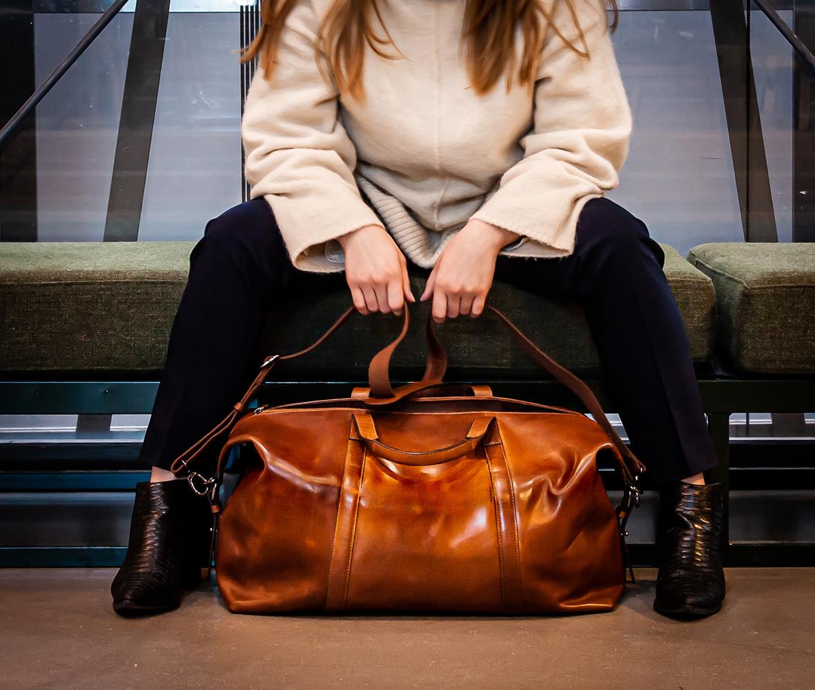Person som sitter med en brun skinn weekendbag Pisa Cognac på golvet