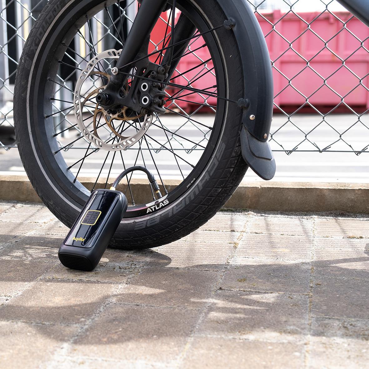 Batteridriven luftpump Aqiila Airbird C4 används för att pumpa cykeldäck, placerad på marken bredvid cykelhjul