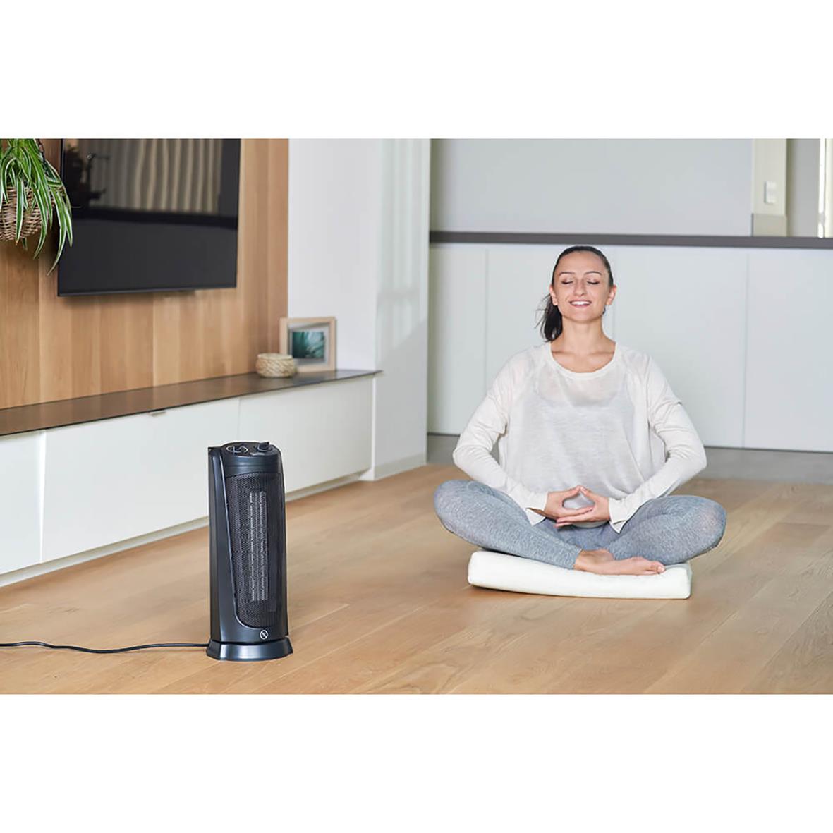 Kvinna mediterar på golvet bredvid en svart keramisk tornvärmare 2000W i ett modernt hem