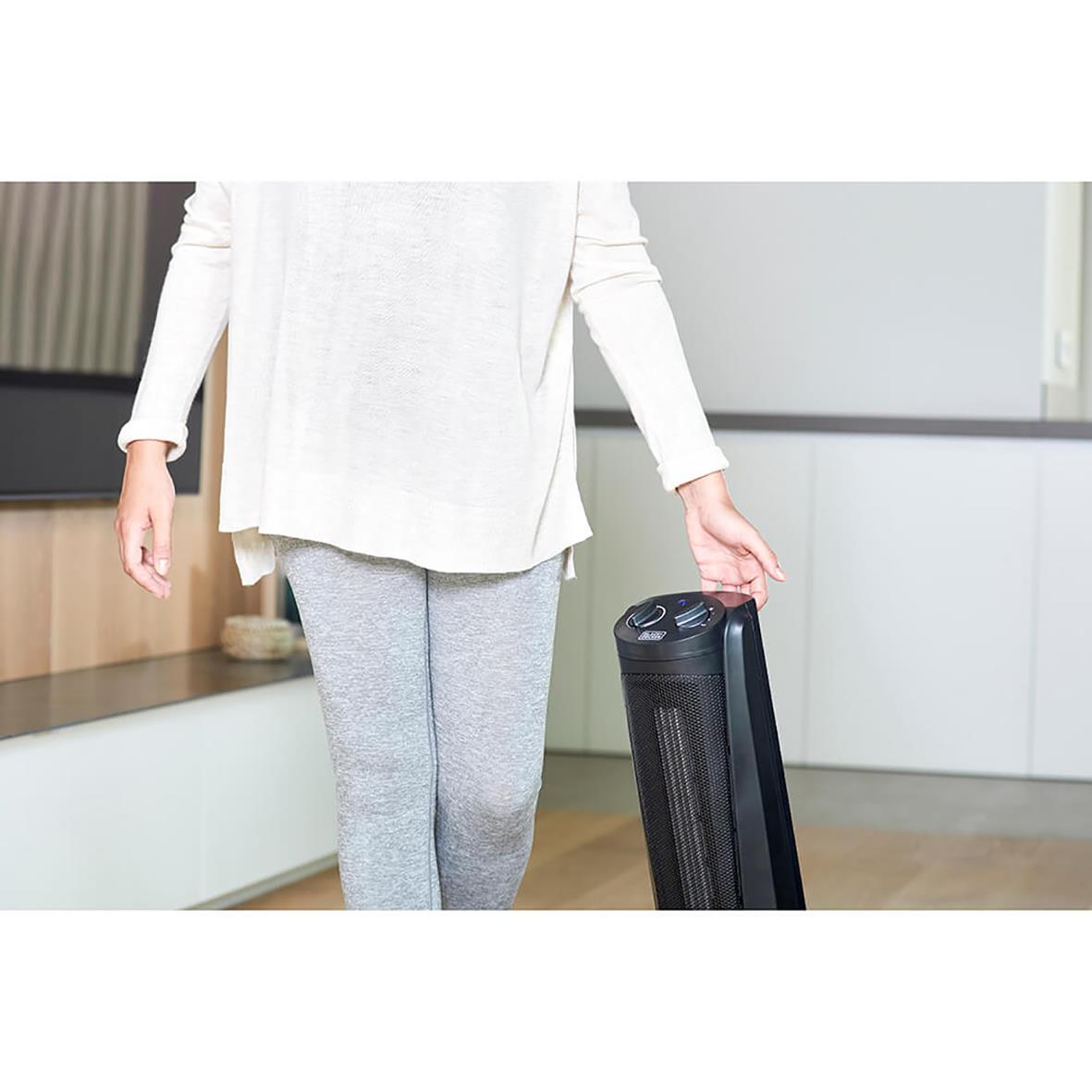 Person som håller i en svart keramisk tornvärmare Black+Decker 2000W i ett hemkök eller vardagsrum