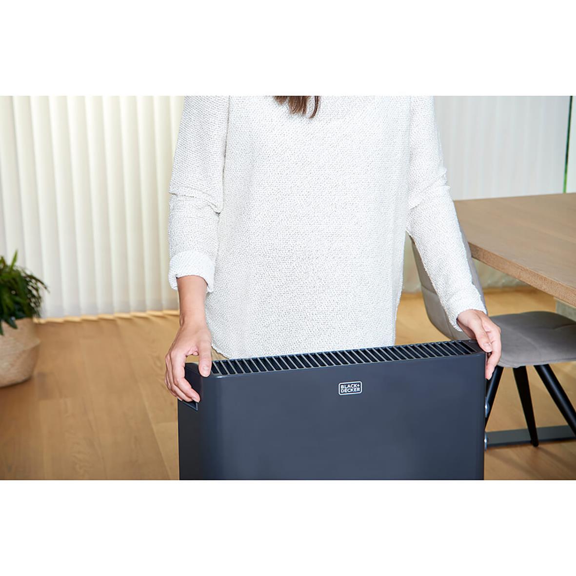 Person som håller i ett svart konvektorelement Black+Decker 2000W i ett rum med träbord och väggpanel
