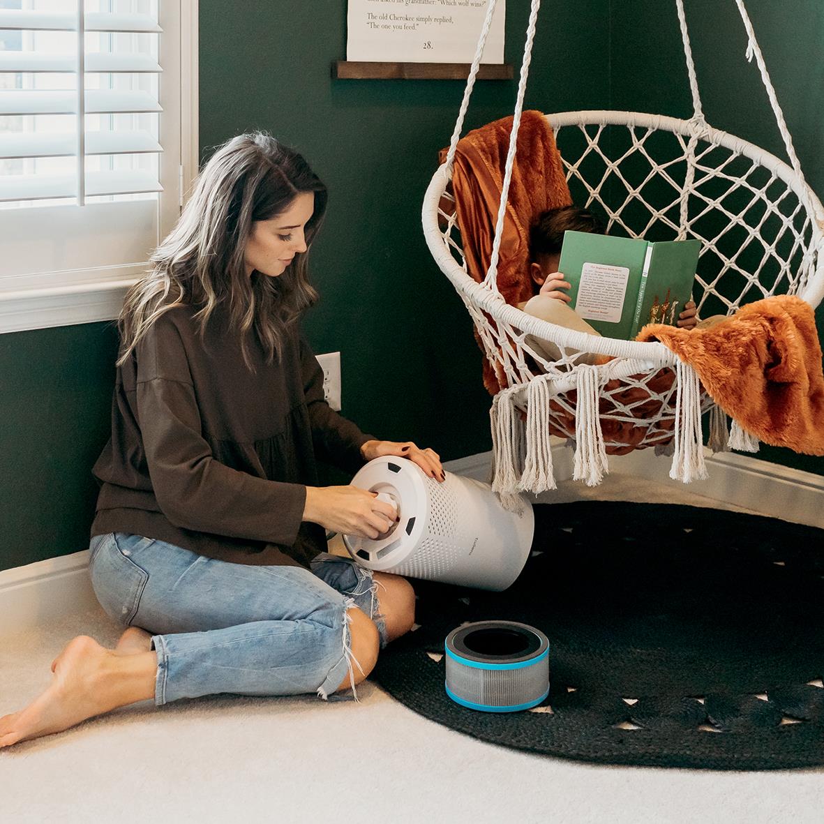 Kvinna byter kolfilter i luftrenare Z-1000 i ett hem med gröna väggar och hängstol