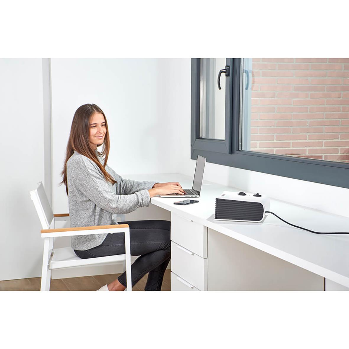 Kvinna vid skrivbord med svart värmefläkt Black+Decker 2000W Platt Vit bredvid fönster