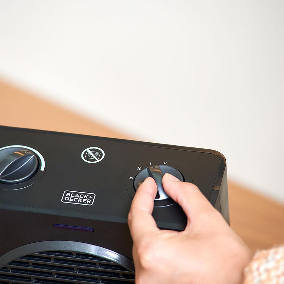 Person justerar värmeinställningen på en svart keramisk värmefläkt från Black+Decker