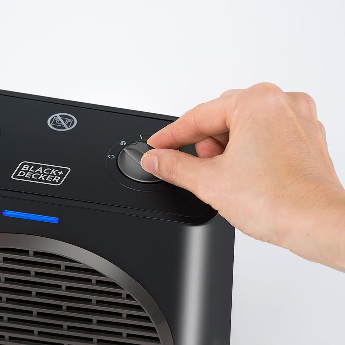 Hand justerar värmeinställning på svart keramisk värmefläkt från Black+Decker