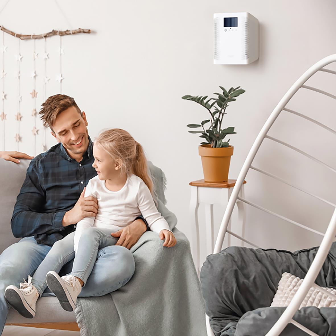 Man och barn leker och skrattar i ett vardagsrum med luftrenare Ozoneair Purify 30 på väggen