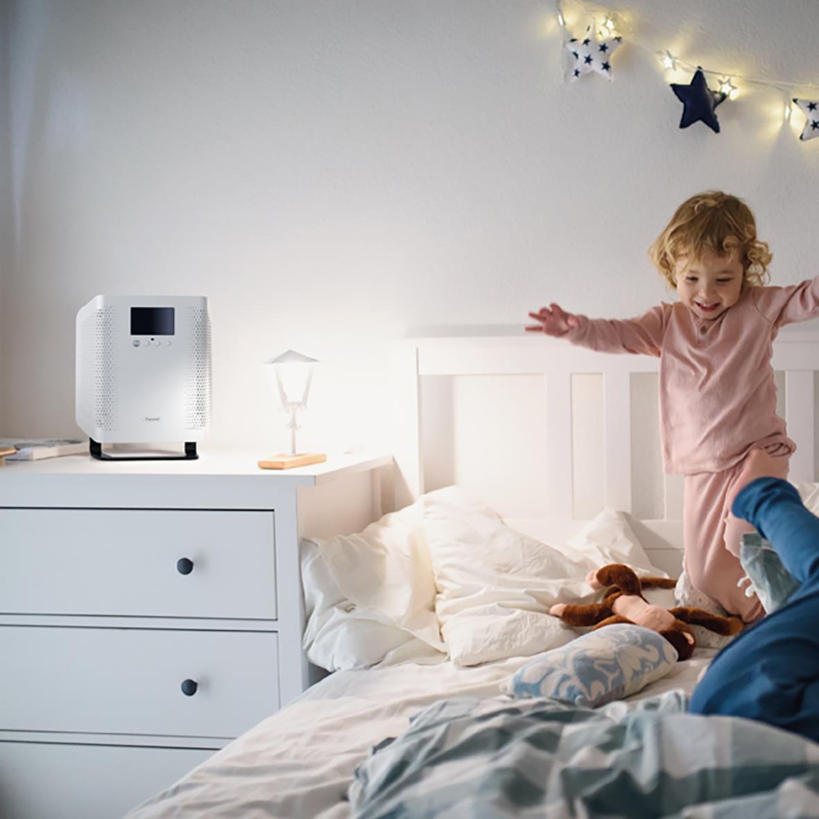 Barn leker på säng med luftrenare Ozoneair Purify 60 i bakgrunden, mysig sovrumsmiljö med julstjärnor och stjärndekorationer