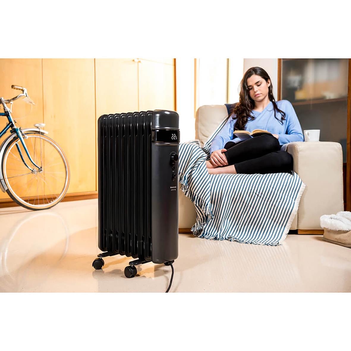 Svart Element Taurus oljefyllt radiator Agadir 2000W placerad i ett vardagsrum med en kvinna som läser på soffan