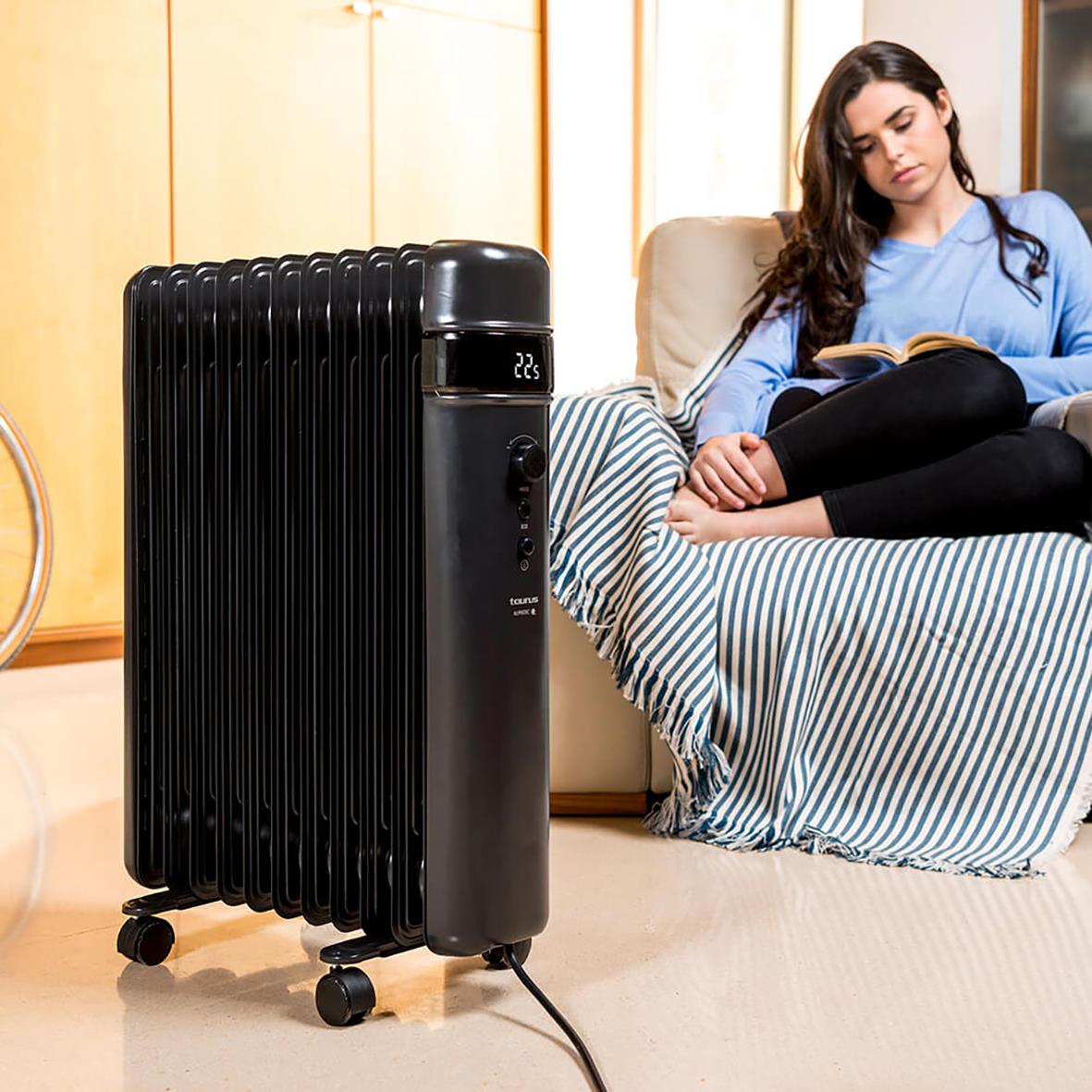 Svart oljeradiator Element Taurus Agadir 2500W placerad i ett vardagsrum med en kvinna som läser på soffan