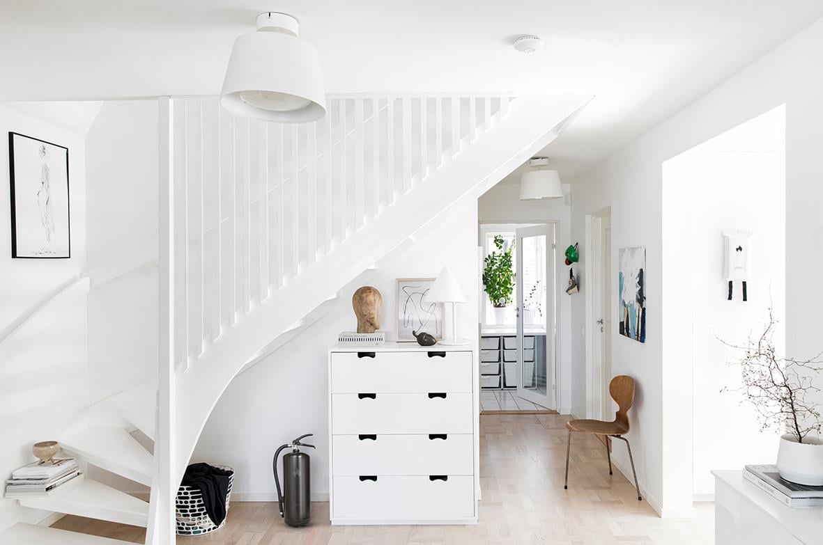 Interiörbild av ett vitt rum med brandsläckare Housegard Pulver Svart 6kg under en trappa