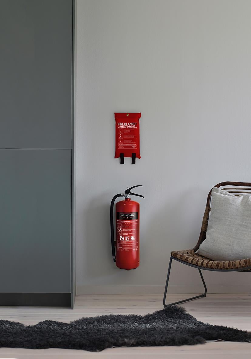 Brandfilt Housegard Röd brandfilt och brandsläckare på vägg i rum med stol och matta