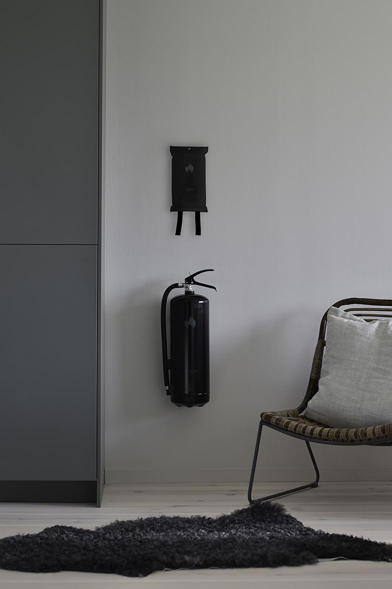 Brandfilt Housegard Design Edition svart brandfilt på vägg bredvid stol och garderob