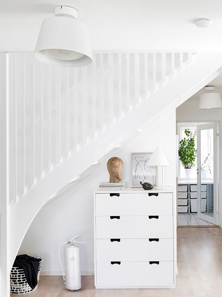 Vit brandsläckare Housegard Pulver 6kg placerad under en vit trappa i ett ljust hem