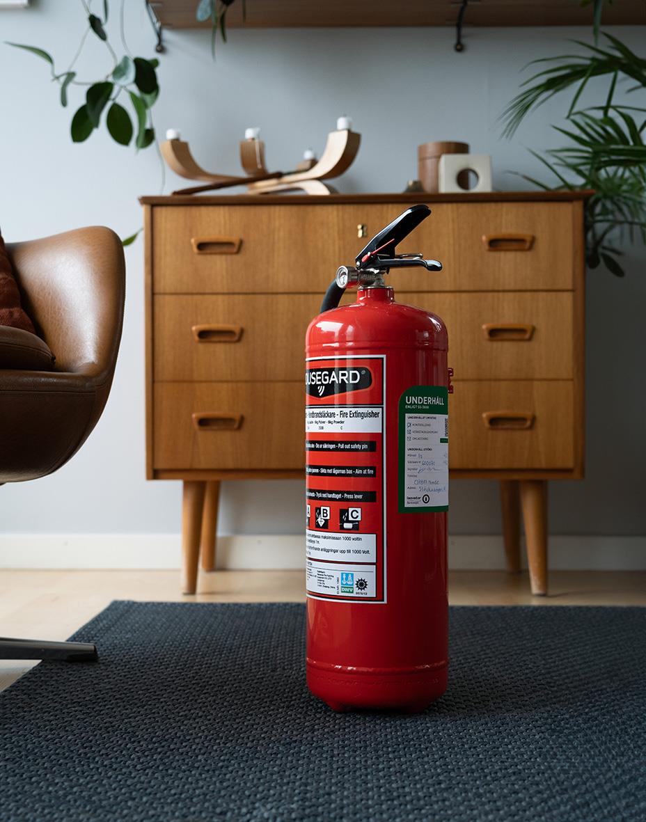 Brandsläckare Housegard Pulver ReUse Röd 6kg stående framför en träskänk i ett vardagsrum