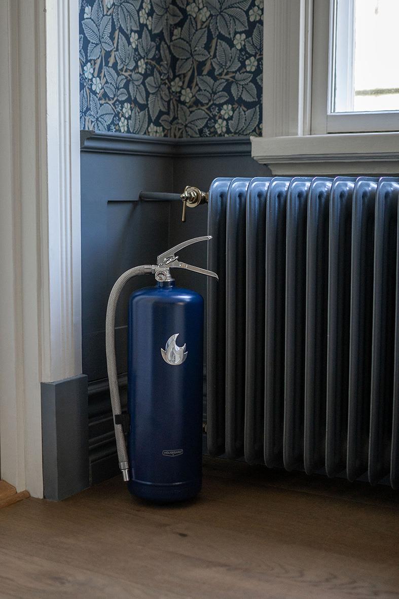Blå pulverbrandsläckare Housegard 6kg placerad bredvid radiator i ett rum med blå vägg och blommig tapet