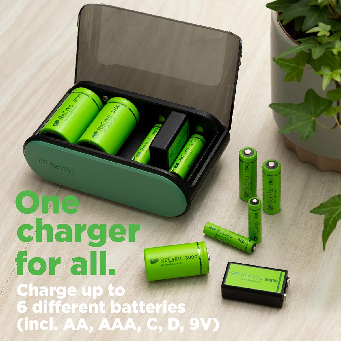 Batteriladdare GP Recyko Universal med gröna uppladdningsbara batterier och laddare på ett bord med växt i bakgrunden