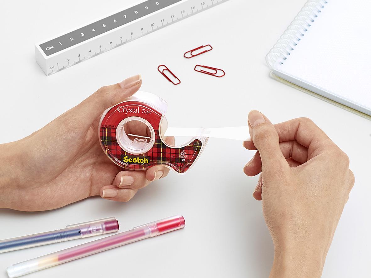 Person använder Scotch 600 Crystal kontorstejp med hållare på skrivbord med pennor, klipp och anteckningsbok