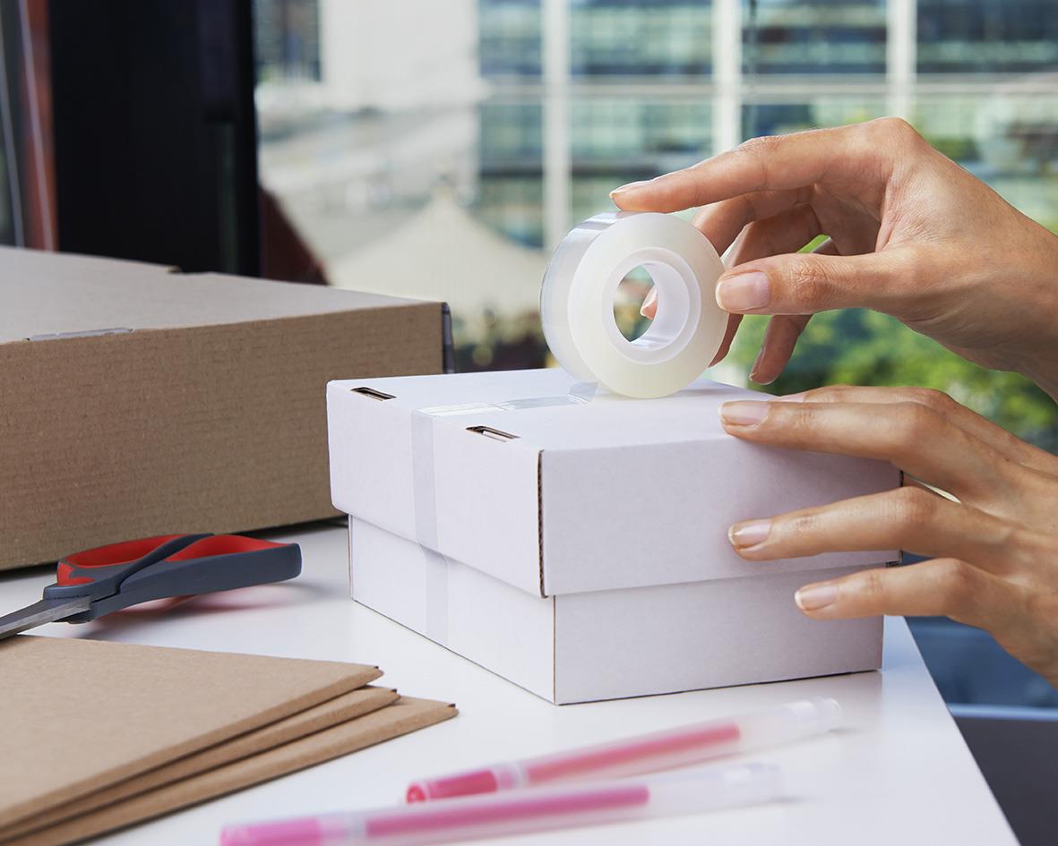 Person använder kontors tejp Scotch 600 Crystal med hållare på en vit skrivbord