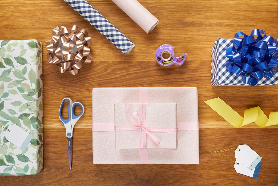 Presentinslagning med transparent Scotch gift-wrap tejp, present, sax, band och paket på träbord