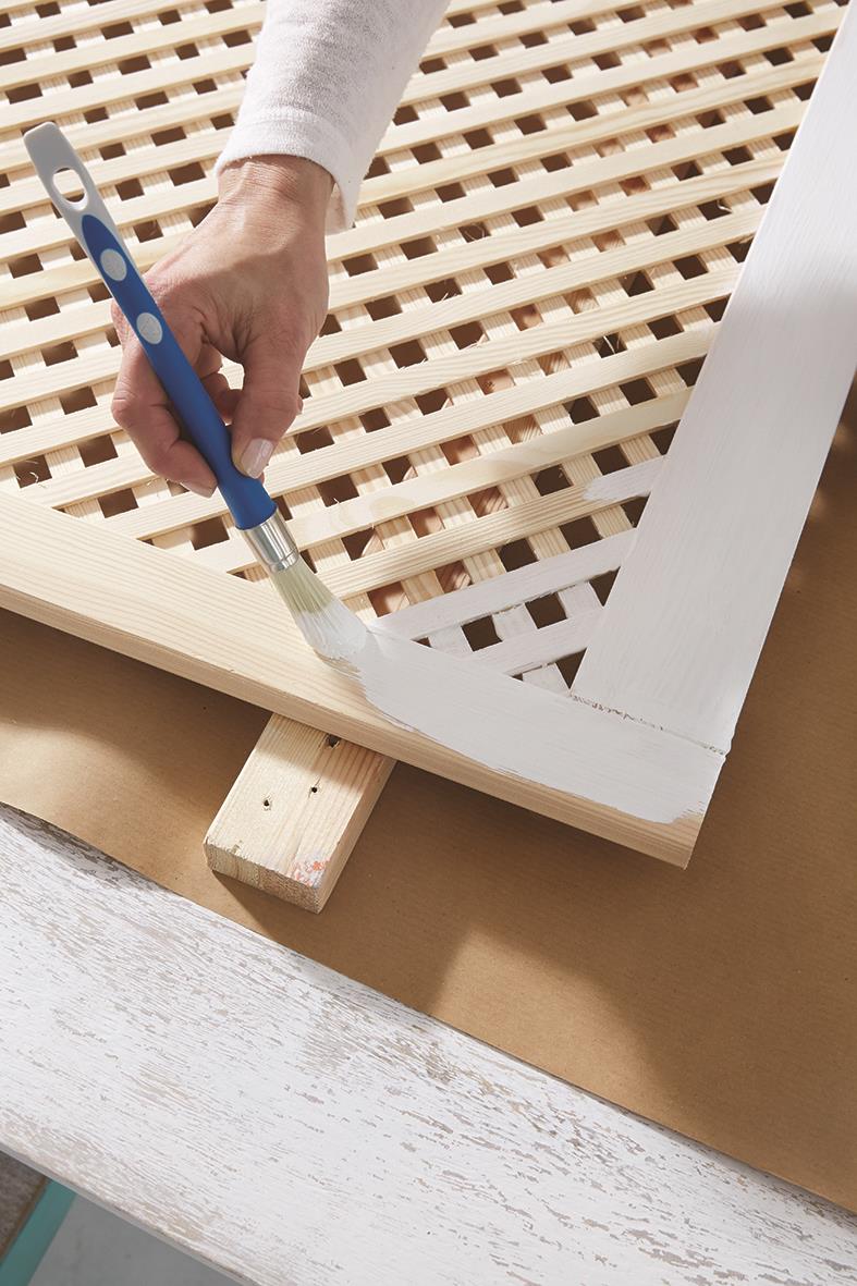 Person målar en träbit med vit färg med pensel på ett bygge eller renoveringsprojekt