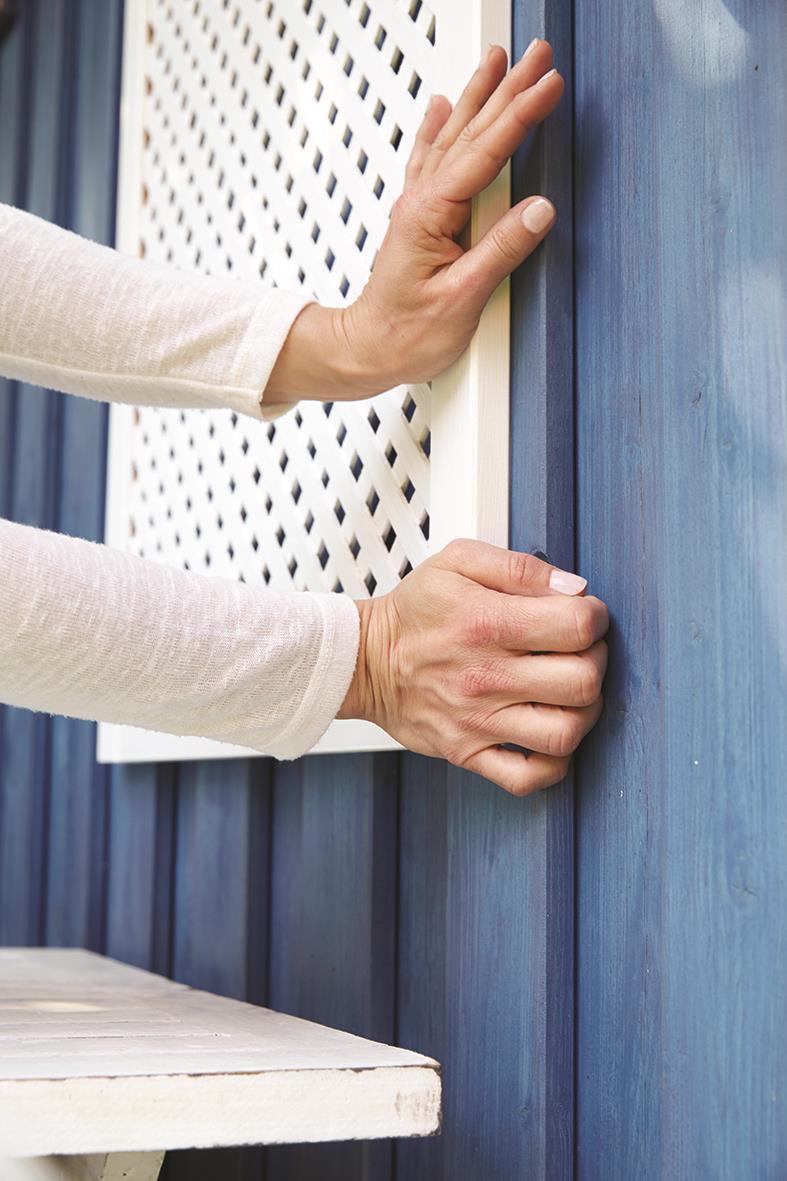 Person som monterar en vit träpanel på en blå vägg med monteringstejp