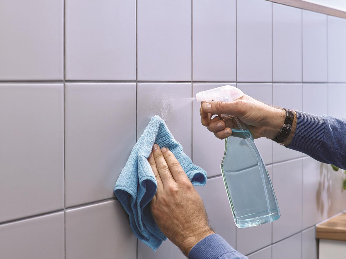Person rengör kakelvägg med sprayflaska och trasa för att förbereda för självhäftande spik